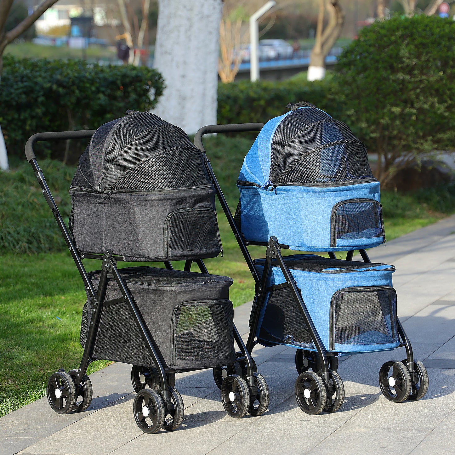 Two pet strollers, one black and one blue, on a sidewalk with greenery in the background.