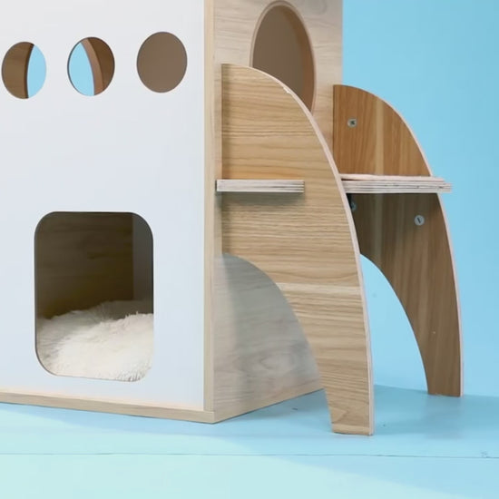 Wooden rocket-ship shaped cat play tower with a cat inside in a modern room setting