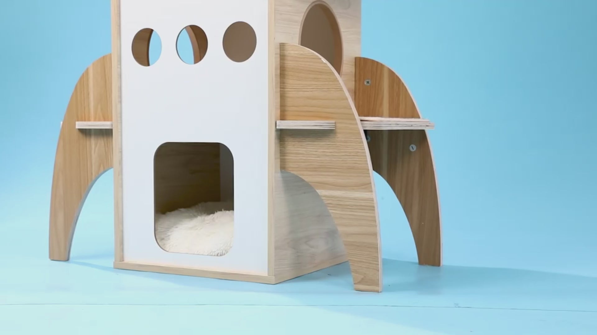 Wooden rocket-ship shaped cat play tower with a cat inside in a modern room setting